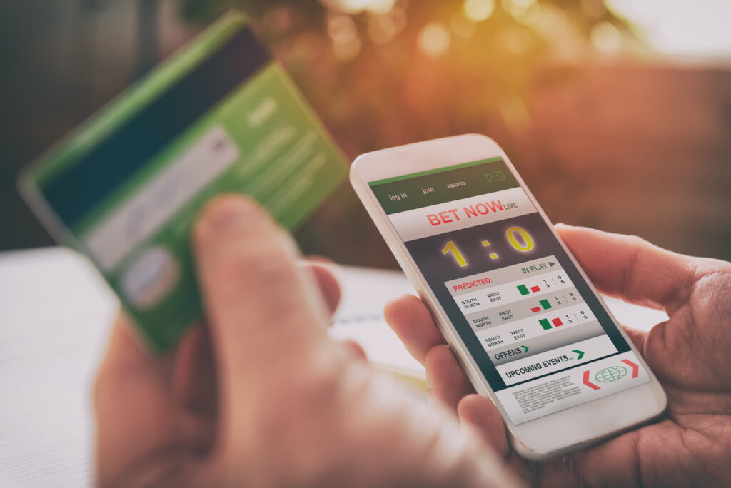 Man betting on sports with credit card, over shoulder view on hand with smartphone